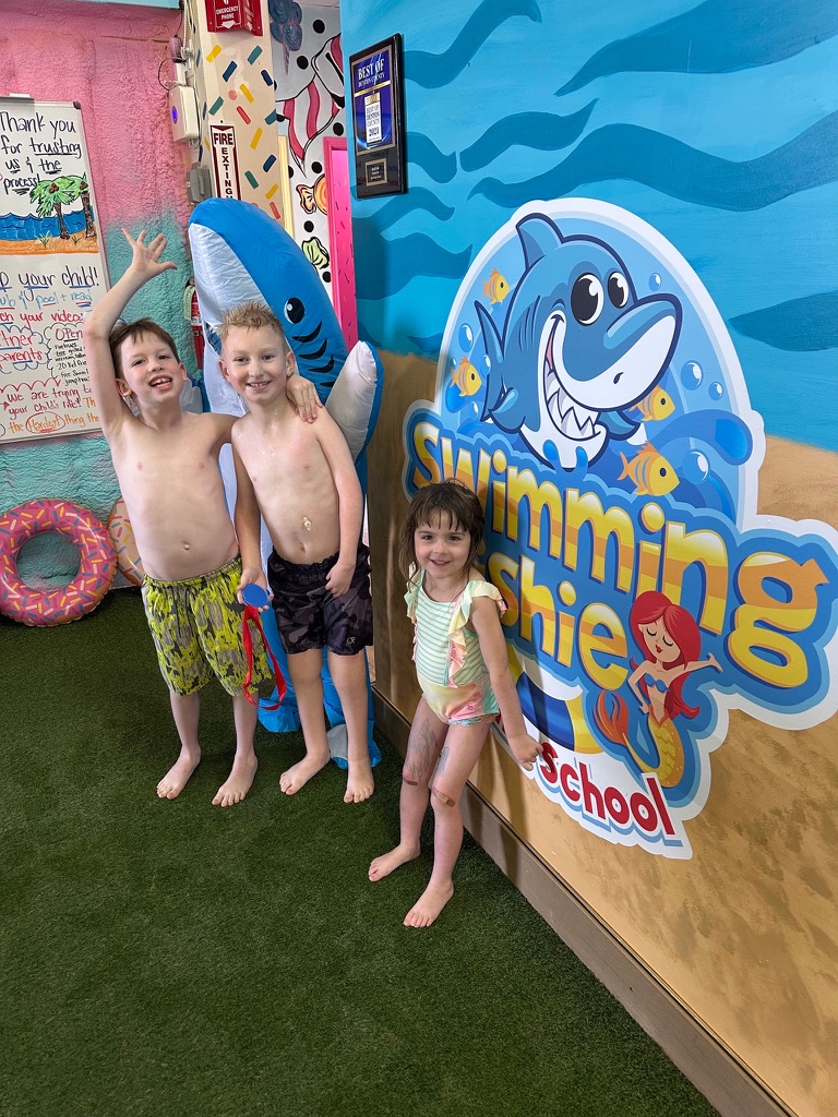 Children posing by the Swimming Fishies logo after lessons